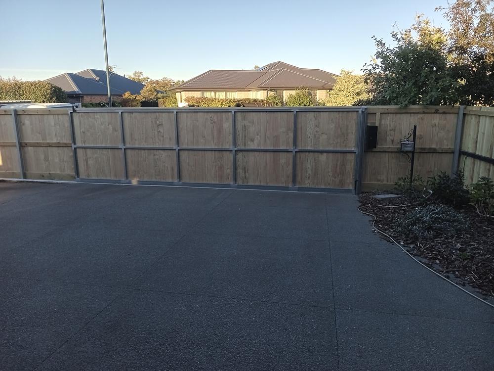 Timber clad sliding gate on a galvanised steel frame across a sealed driveway